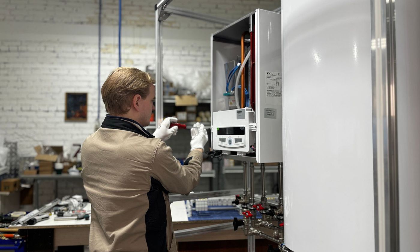 Technician working on the control panel of a wall-mounted water heater beside a storage tank
